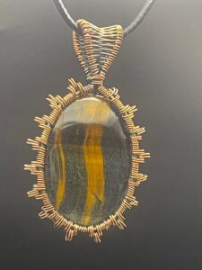 Hand-wrapped copper wire pendant featuring an oval cabochon of shimmering tiger's eye in rich honey and dark brown tones.